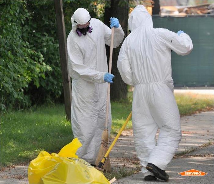 two men in white hazmat suits outside raking things into a bag