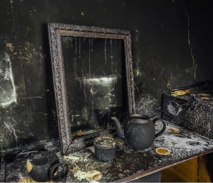 Fire damaged desk with mirror, walls black, teapot resting on desk is covered with soot, black and white soot, SERVPRO