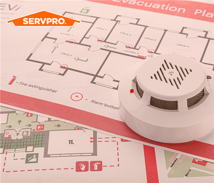 fire safety evacuation plan map with a smoke detector sitting on top of it, SERVPRO orange house logo